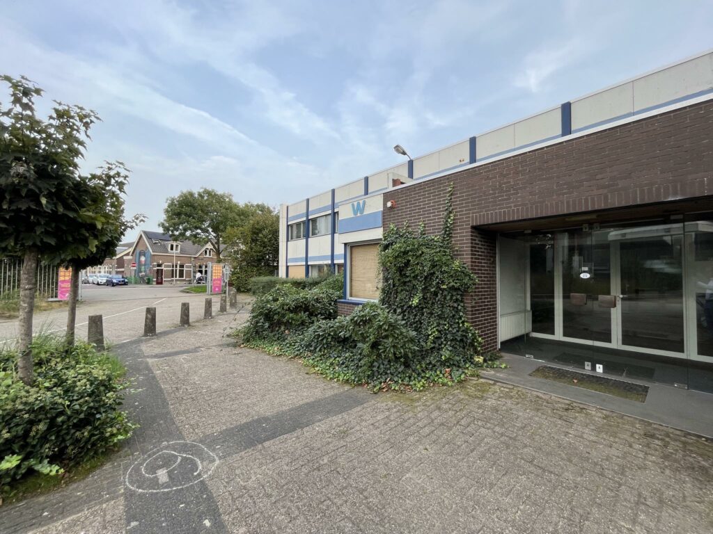 Entree van een leegstaand bedrijfsgebouw aan de 2e Daalsedijk met een betegeld pad en overwoekerde planten.